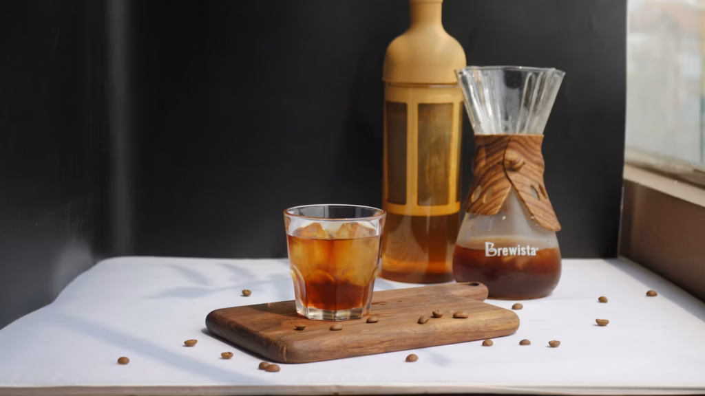 Vaso de café frío con hielo junto a granos y jarra de café