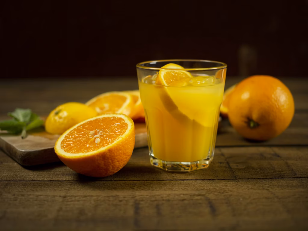 Jugo de naranja natural servido junto a naranjas frescas