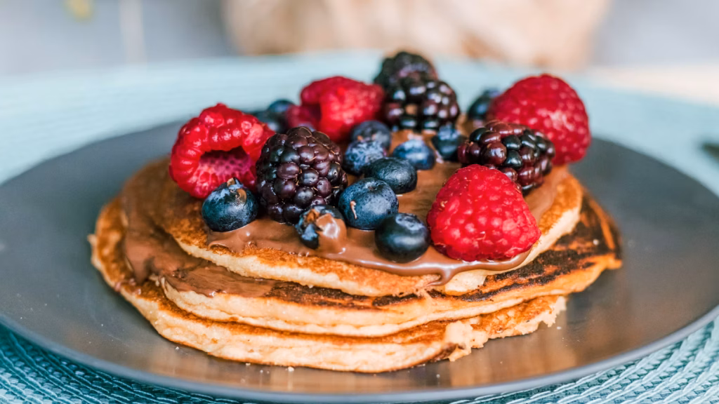 Pila de hot cakes con frutos rojos sobre un plato azul