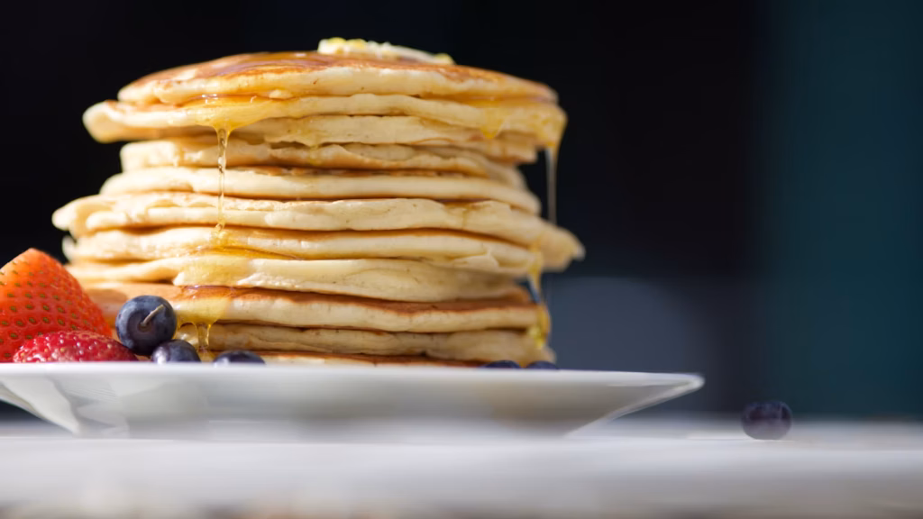 Hot cakes con jarabe, fresas y arándanos en un plato blanco